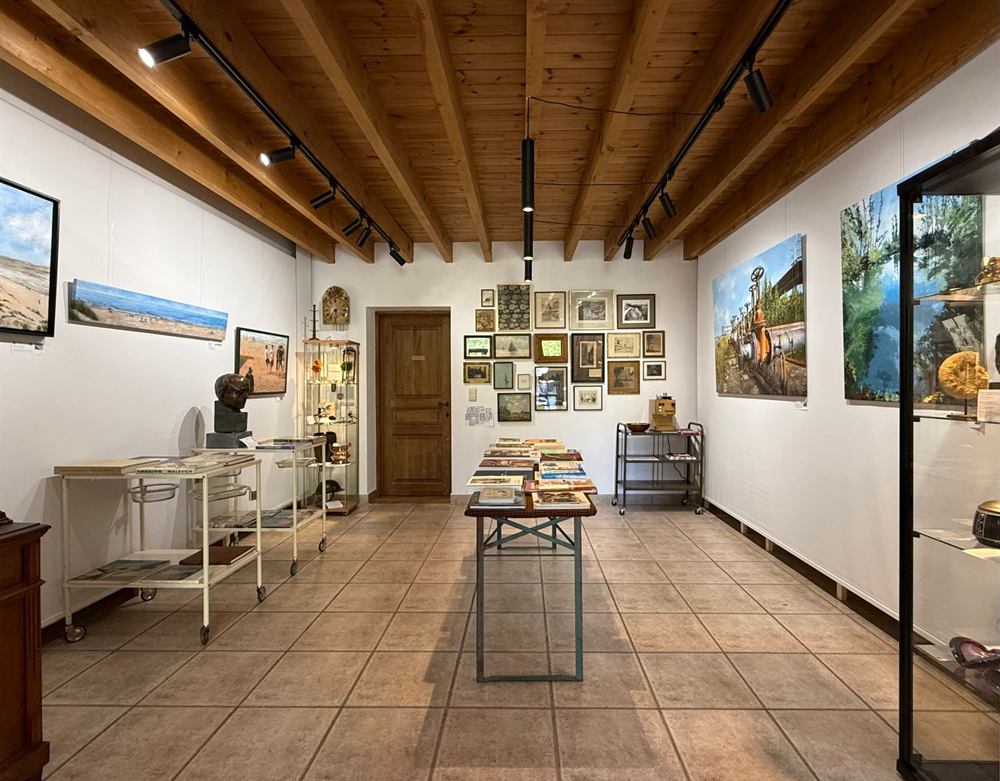 Een witte galerieruimte met schilderijen, een vitrinekast en een wand vol ingelijste prenten